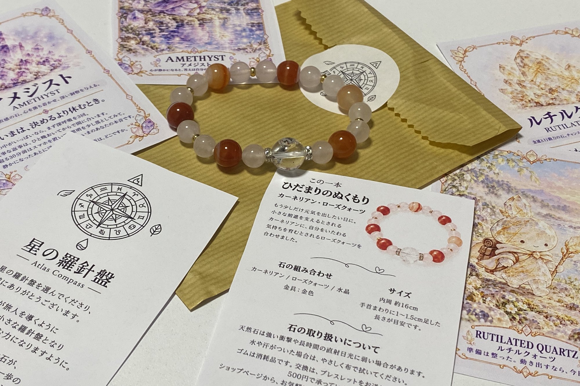 ロゴのシールを貼った金色の紙袋の上にブレスレット。まわりに同封のカードを並べたところ。